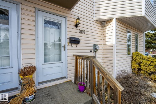 The property features a front entrance with a white storm door, accented by a wall-mounted light fixture and house numbers - 2006 Mill Woods Road E, Edmonton, AB - Outdoor With Exterior