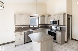Kitchen featuring a central island, light wood-finish cabinetry, stainless steel appliances, and a double basin sink - 