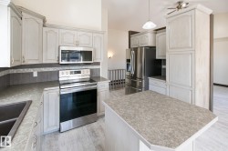 Kitchen featuring light-toned cabinetry, stainless steel appliances, a center island with a speckled countertop, a dual-basin sink, and wood-finish flooring - 