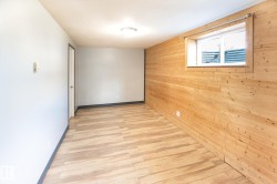 Room featuring natural wood paneling, wood-finish flooring, a flush-mount ceiling light, and a window with a white frame - 