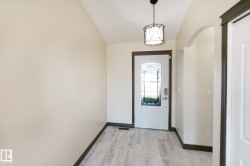 Entryway featuring wood-finish flooring, a decorative pendant light fixture, an arched doorway, and a white entry door with frosted glass detailing - 