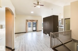 Spacious interior featuring light wood-finish flooring, a ceiling fan, vaulted ceilings, and a light-filled kitchen with a window - 