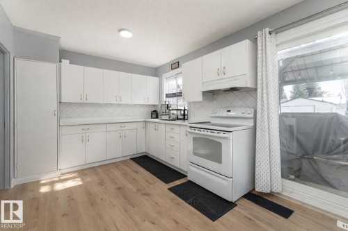 Kitchen featuring light wood tone flooring, white cabinetry, a white tile backsplash, and a white electric range - 16131 109 Avenue, Edmonton, AB - Indoor Photo Showing Kitchen
