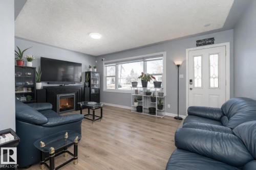 Living room featuring light-colored flooring, a fireplace with a dark mantel, and a large window providing natural light - 16131 109 Avenue, Edmonton, AB - Indoor Photo Showing Living Room With Fireplace