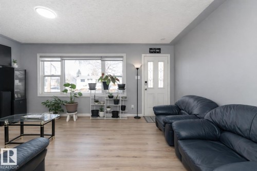 The interior features light-colored flooring, windows providing natural light, and a white entry door with decorative glass inserts - 16131 109 Avenue, Edmonton, AB - Indoor Photo Showing Living Room