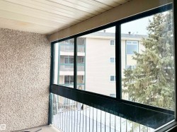 The property features an enclosed balcony with large windows, offering a view of nearby buildings and mature trees - 