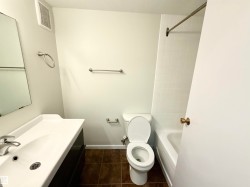 The bathroom features a vanity with an integrated sink, a toilet, a bathtub with white subway tile surround, and brown tiled flooring - 