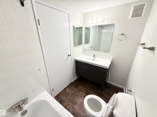 The bathroom features a vanity with a rectangular sink, a toilet, a bathtub with white tiled walls, and a wall-mounted mirror - 307 1620 48 Street, Edmonton, AB - Indoor Photo Showing Bathroom