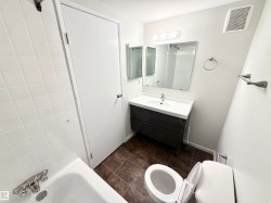 The bathroom features a vanity with a rectangular sink, a toilet, a bathtub with white tiled walls, and a wall-mounted mirror - 