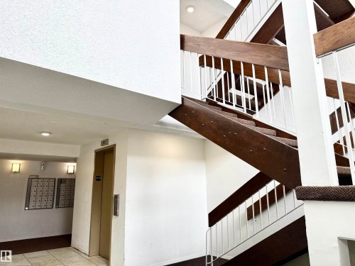 The building features a well-maintained staircase with dark wood and white railings, complemented by an elevator for convenience - 307 1620 48 Street, Edmonton, AB - Indoor Photo Showing Other Room