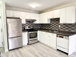 The kitchen features white cabinetry, a stainless steel refrigerator, and a stainless steel oven with a range hood - 