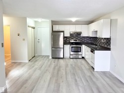Kitchen and living area featuring light-toned flooring, white cabinetry, stainless steel appliances, and a tiled backsplash - 