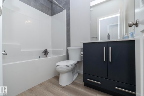 Bathroom featuring a white bathtub, a toilet, a vanity with a dark cabinet, and light-colored flooring - 159 Larch Crescent, Leduc, AB - Indoor Photo Showing Bathroom