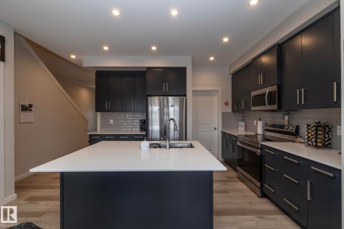 This contemporary kitchen boasts dark cabinetry, stainless steel appliances, a large center island with a sink, and light-colored countertops - 159 Larch Crescent, Leduc, AB - Indoor Photo Showing Kitchen With Upgraded Kitchen