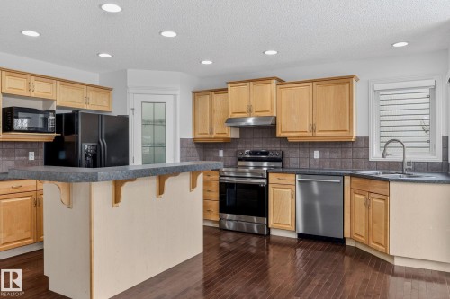The kitchen features wooden cabinetry, dark countertops, and stainless steel appliances - 978 Rutherford Road Sw, Edmonton, AB - Indoor Photo Showing Kitchen With Double Sink