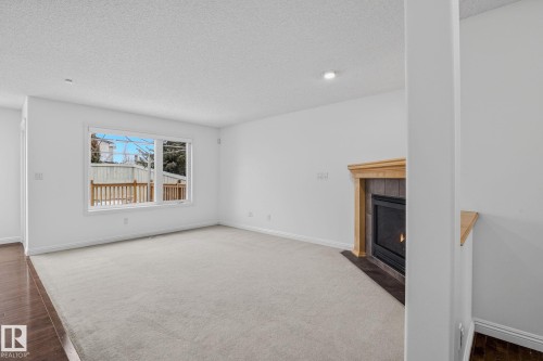 The living area features a large window with views of a wooden deck, a fireplace with a light wood mantel and dark tile surround, and light-colored carpeting - 978 Rutherford Road Sw, Edmonton, AB - Indoor Photo Showing Living Room With Fireplace