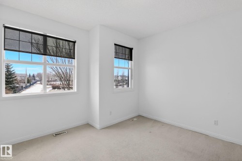 This room features light-colored carpet, white walls, and two windows providing views of the neighborhood - 978 Rutherford Road Sw, Edmonton, AB - Indoor Photo Showing Other Room