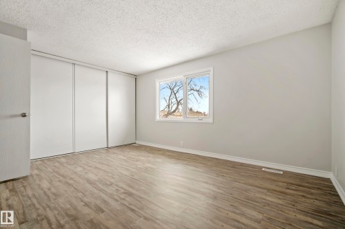 This room features light wood-style flooring, a window with a view of trees, and a spacious closet with sliding doors - 3311 139 Avenue, Edmonton, AB - Indoor Photo Showing Other Room