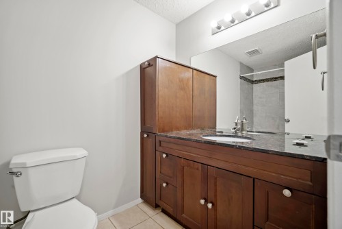 Bathroom featuring a dark wood vanity with a dark countertop and an integrated sink, a large mirror, and a toilet - 3311 139 Avenue, Edmonton, AB - Indoor Photo Showing Bathroom
