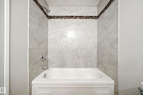 The bathroom features a tiled shower and bathtub combination with a decorative mosaic tile accent band - 3311 139 Avenue, Edmonton, AB - Indoor Photo Showing Bathroom