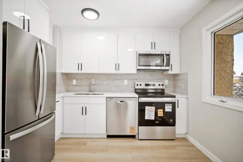 The kitchen features white cabinetry, stainless steel appliances including a refrigerator, microwave, and range, light-toned countertops, and a window providing natural light - 3311 139 Avenue, Edmonton, AB - Indoor Photo Showing Kitchen With Stainless Steel Kitchen