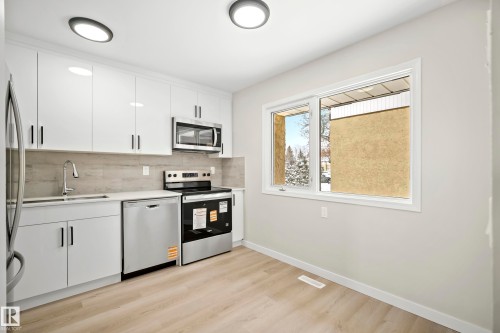 The kitchen features white cabinetry with modern handles, stainless steel appliances, and a light-colored wood floor - 3311 139 Avenue, Edmonton, AB - Indoor Photo Showing Kitchen With Stainless Steel Kitchen