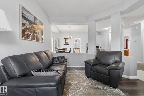 The living area features light grey walls, dark wood-look flooring, and an archway opening into a dining area with a window - 17204 113 Street, Edmonton, AB - Indoor Photo Showing Living Room