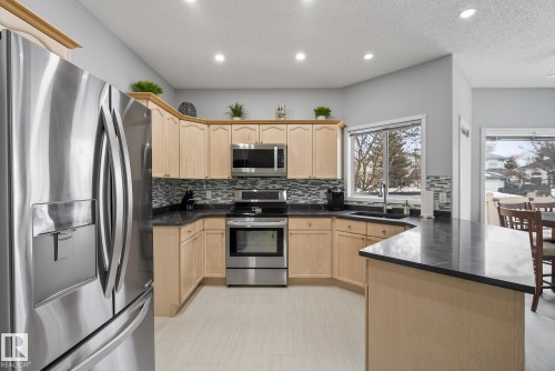 The kitchen features a stainless steel refrigerator, range, and microwave, complemented by light wood cabinetry and dark countertops - 17204 113 Street, Edmonton, AB - Indoor Photo Showing Kitchen