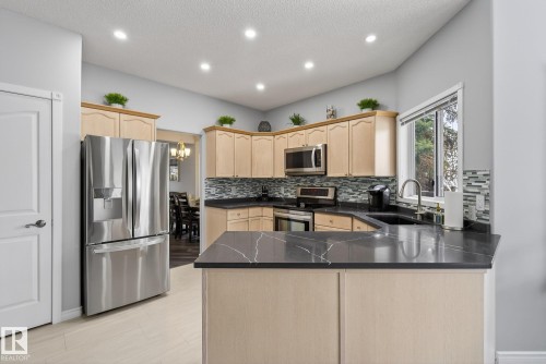 The kitchen features light wood cabinetry, stainless steel appliances, dark countertops with light veining, and a tiled backsplash - 17204 113 Street, Edmonton, AB - Indoor Photo Showing Kitchen