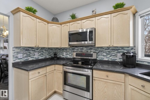 The kitchen features ample light wood cabinetry, dark countertops, a tiled backsplash, and stainless steel appliances including a range and microwave - 17204 113 Street, Edmonton, AB - Indoor Photo Showing Kitchen