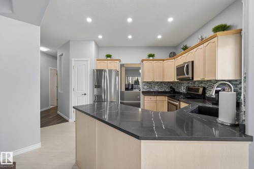 The kitchen features light-toned cabinetry, stainless steel appliances, a dark countertop with light veining, and a patterned backsplash - 17204 113 Street, Edmonton, AB - Indoor Photo Showing Kitchen