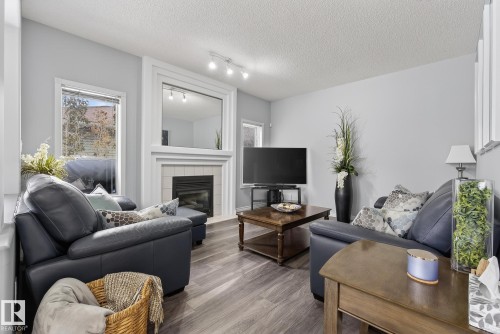 The living room features wood-style flooring, a fireplace with a tiled surround and white mantel, and a large mirror above the fireplace - 17204 113 Street, Edmonton, AB - Indoor Photo Showing Living Room With Fireplace