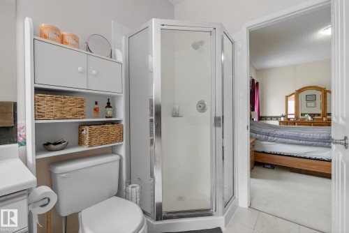The bathroom features a toilet with an overhead storage unit, a corner shower with a glass enclosure, and tiled flooring - 17204 113 Street, Edmonton, AB - Indoor Photo Showing Bathroom