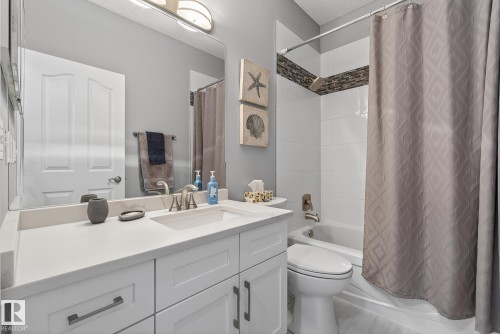 Bathroom featuring a white vanity with a light-colored countertop, a shower-tub combination with white tile surround, and a decorative tile accent band in the shower - 17204 113 Street, Edmonton, AB - Indoor Photo Showing Bathroom