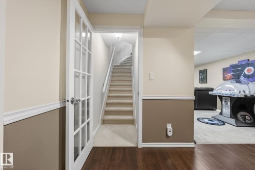 Finished basement area featuring wood-look flooring, a carpeted staircase with white railings, and a doorway with white French doors - 17204 113 Street, Edmonton, AB - Indoor Photo Showing Other Room