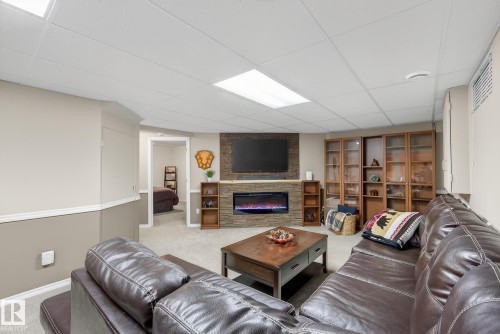 Living space featuring a stone-clad fireplace with an electric insert, a television mounted above, and built-in wooden shelving units - 17204 113 Street, Edmonton, AB - Indoor Photo Showing Other Room