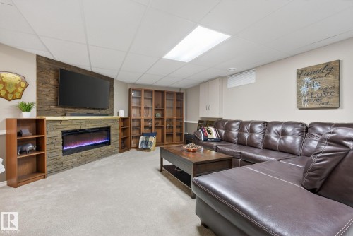 Living area featuring carpeted flooring, a stone-accented media wall with an electric fireplace, built-in shelving, and recessed lighting - 17204 113 Street, Edmonton, AB - Indoor Photo Showing Other Room