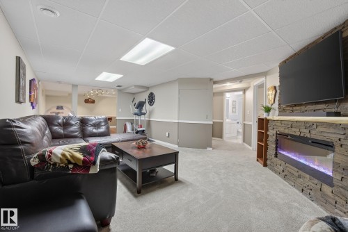 Living area featuring light grey carpeting, a fireplace with a stone surround, and a drop ceiling with recessed lighting - 17204 113 Street, Edmonton, AB - Indoor Photo Showing Living Room With Fireplace