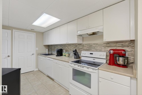 The kitchen features white cabinetry, a tiled backsplash, a built-in range, and a sink with a dark basin - 17204 113 Street, Edmonton, AB - Indoor Photo Showing Kitchen
