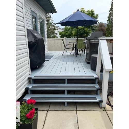 The property features a spacious outdoor deck with light-colored flooring and a three-step staircase leading to a paved patio area - 17204 113 Street, Edmonton, AB - Outdoor