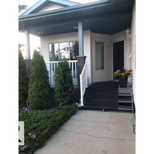 Inviting front entrance featuring a covered porch, stone accents, white railings, and a landscaped garden bed with mature shrubs - 17204 113 Street, Edmonton, AB - Outdoor