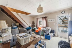The living area features a staircase with a wooden handrail, a window with curtains, and a ceiling light fixture - 