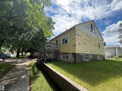 Two-story residence featuring a wood deck with stairs, multiple windows, and a concrete retaining wall - 