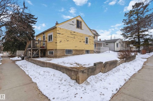 The property features a yellow exterior with white trim, multiple windows, and a raised wooden deck with stairs - 10186 143 Street, Edmonton, AB - Outdoor