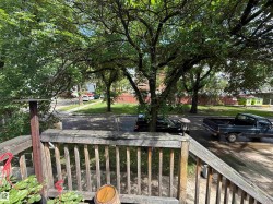 Wooden deck railing overlooking a tree-lined street with mature trees - 