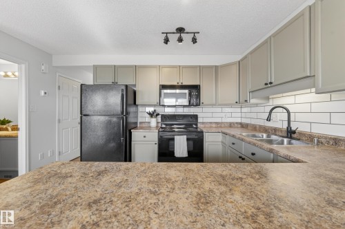 Kitchen featuring a dark countertop, subway tile backsplash, and light-colored cabinetry - 9051 Scott Crescent, Edmonton, AB - Indoor Photo Showing Kitchen With Double Sink