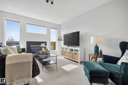 Living room featuring light-colored carpet, a fireplace, and large windows providing natural light - 9051 Scott Crescent, Edmonton, AB - Indoor Photo Showing Living Room With Fireplace