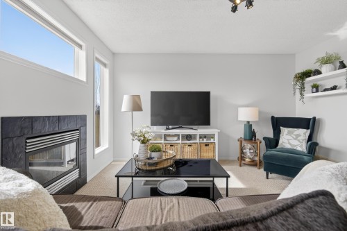 The living area features a built-in fireplace with a dark stone surround, tall windows providing natural light, and track lighting on the ceiling - 9051 Scott Crescent, Edmonton, AB - Indoor Photo Showing Living Room With Fireplace