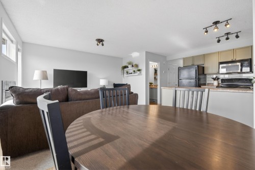 The property offers an open concept living area, featuring a dining space with a round wooden table, a living room with light-colored walls, and a kitchen equipped with a black refrigerator and microwave - 9051 Scott Crescent, Edmonton, AB - Indoor
