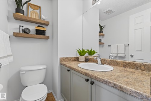 This bathroom features a vanity with a countertop and a white sink, along with a toilet and floating wooden shelves - 9051 Scott Crescent, Edmonton, AB - Indoor Photo Showing Bathroom